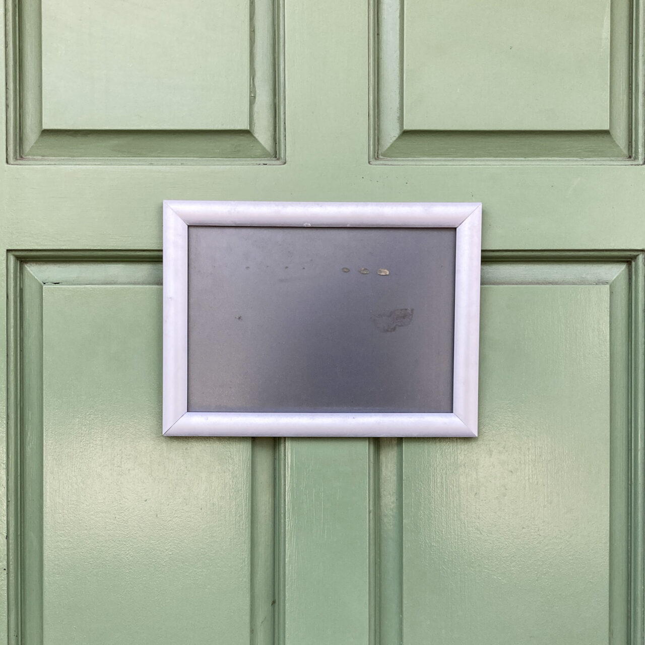 Walton-on-the-Naze. Photograph of an empty frame with just plain black inside, on a green door, of which you can see parts of the four panels.