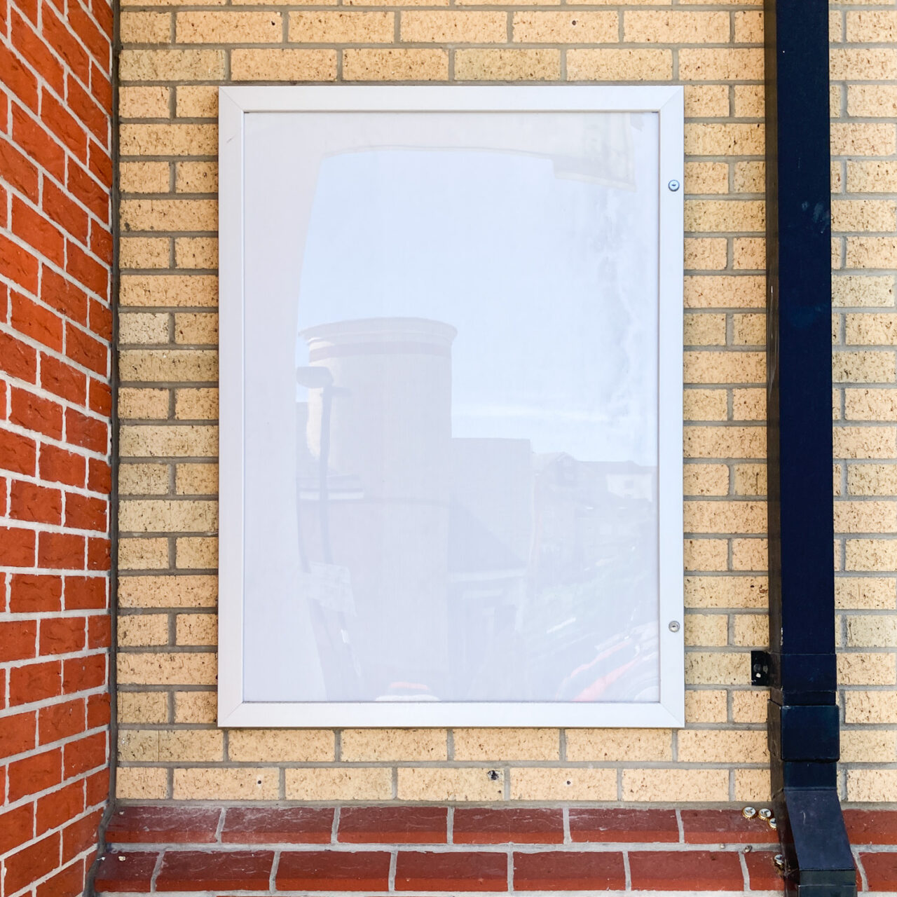 Colchester. Photograph of an empty metal frame on a brick wall with a black pipe to the right.