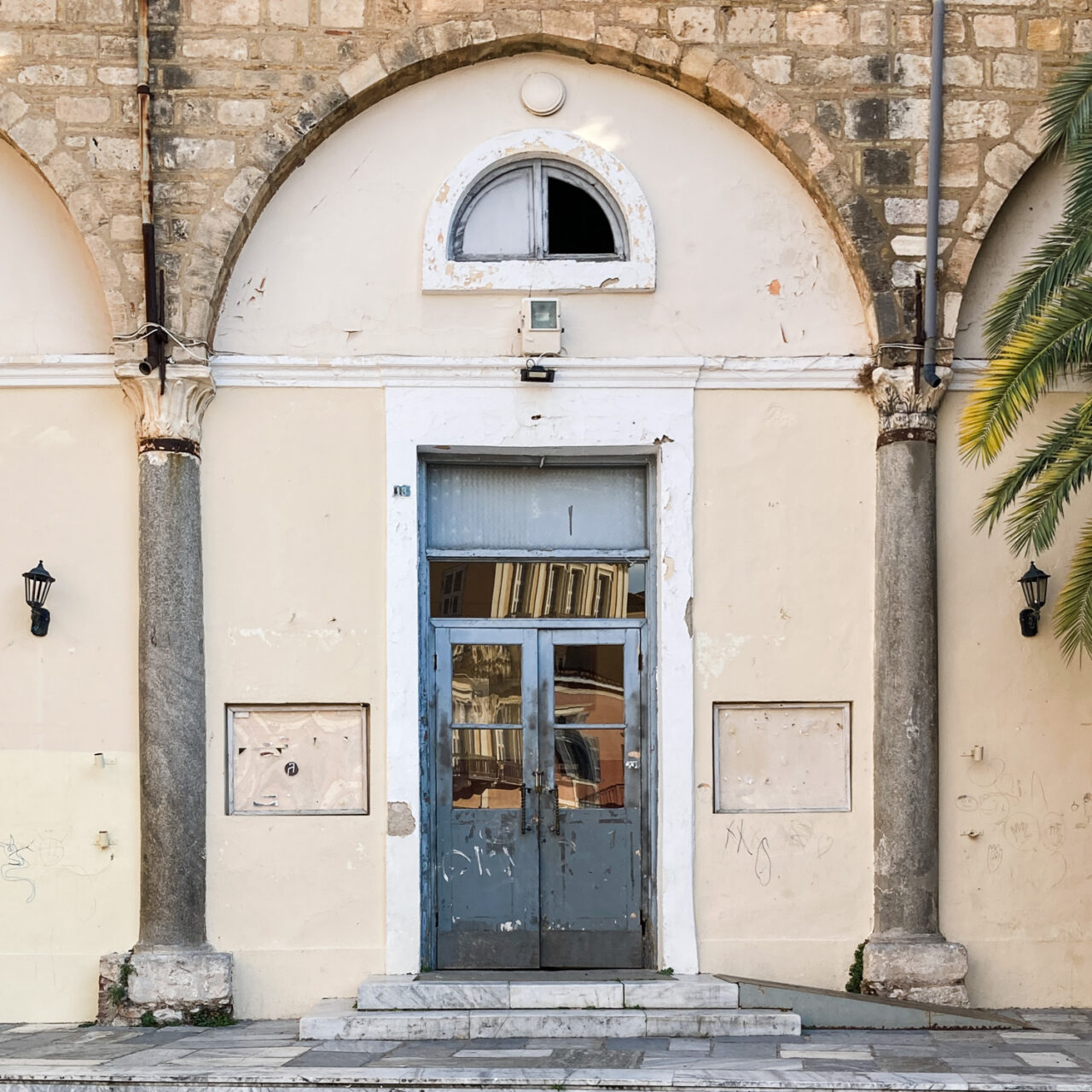 Nafplio. Photograph of two empty display boards either side of a door, with an arch above and columns either side, and tiled floor in front.