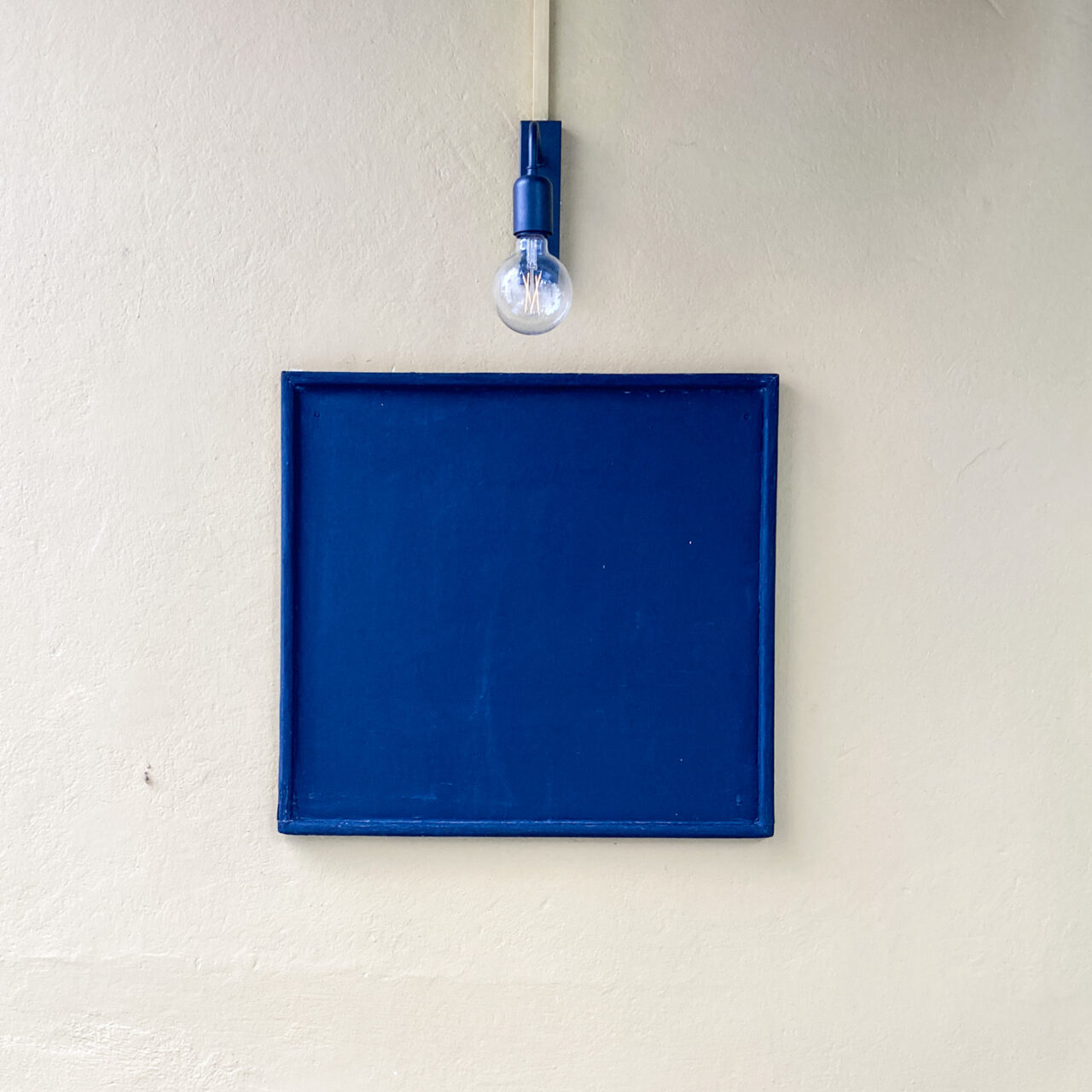 Nafplio. Photograph of an empty blue wooden noticeboard with an old fashioned lightbulb above.