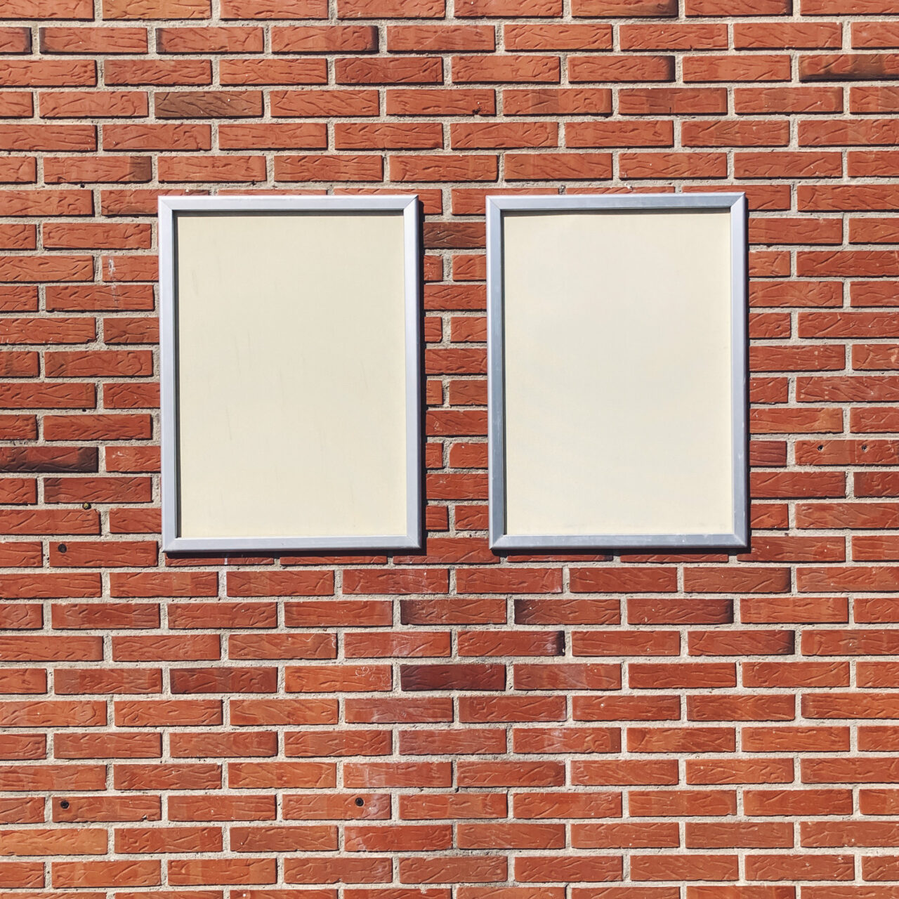 Photograph of two cream noticeboards mounted on a brick wall.